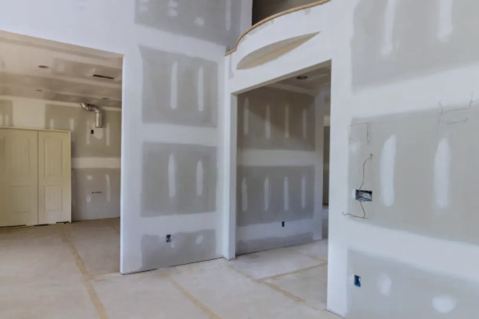 Open-plan interior with walls and a curved archway in taped and mudded drywall, seams and fasteners coated, rosin paper on the floor