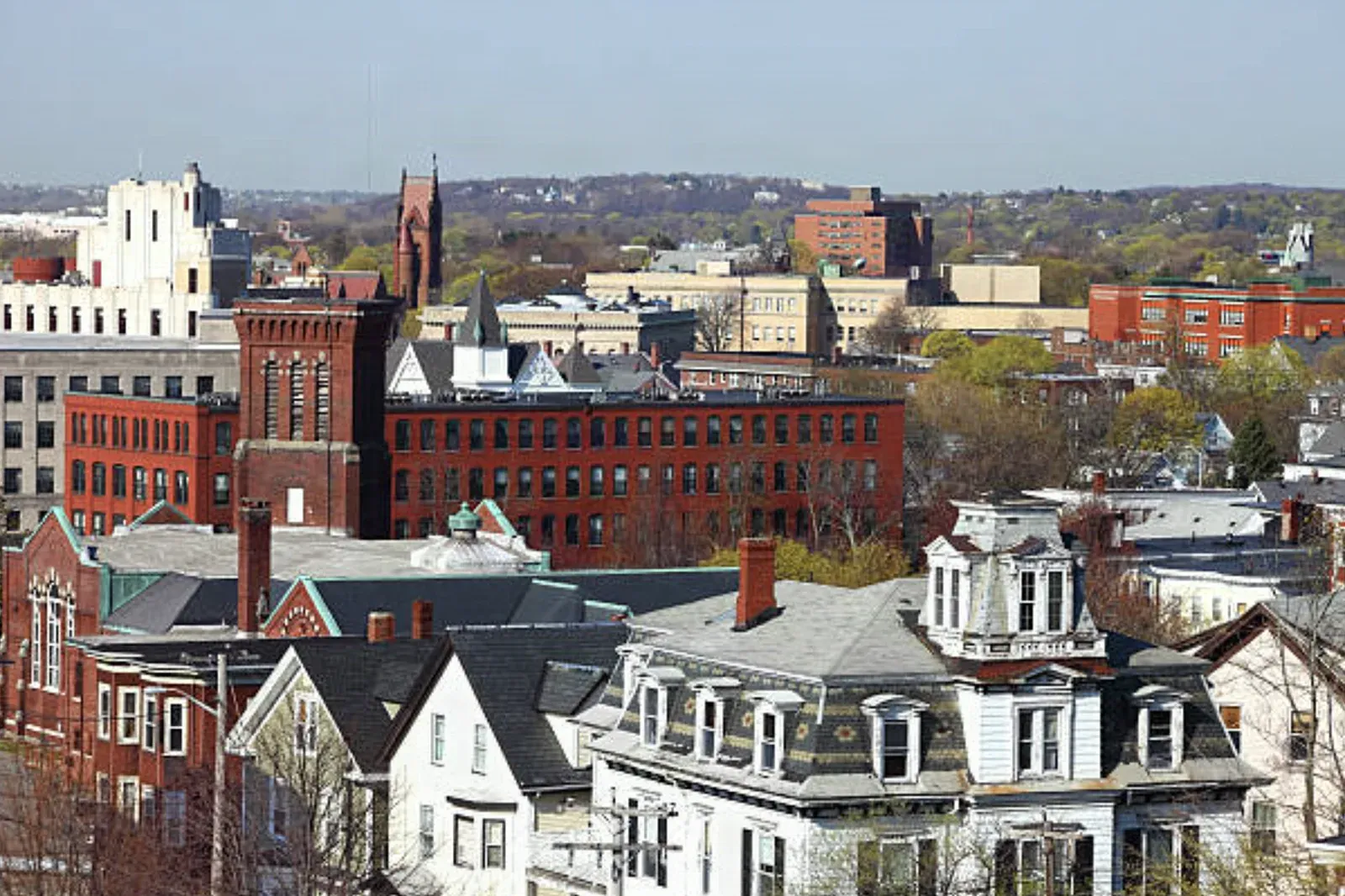 Rooftop view across downtown Lynn, Massachusetts: brick shoe-factory blocks, church spires, and mansard-roofed Victorian houses